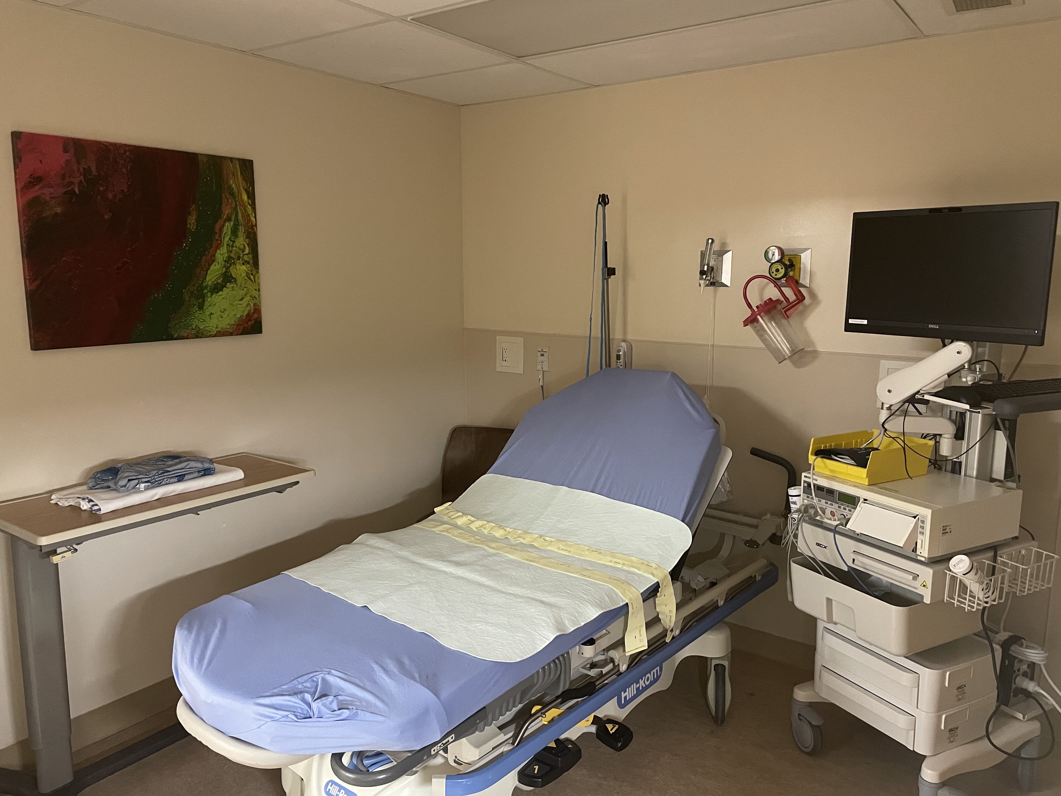 Picture of OB Department Room with bed, table, computer, and colourful art on wall